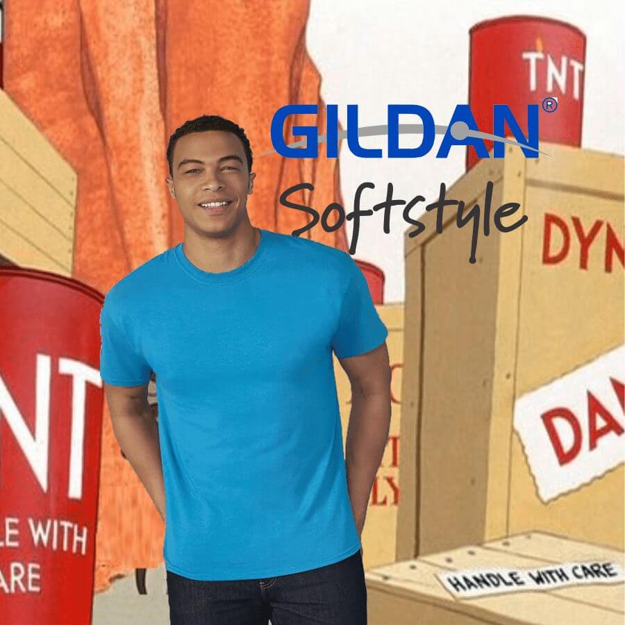64000 Male model wearing a bright blue Gildan Softstyle fitted t-shirt against a cartoon-style background with dynamite crates and TNT barrels