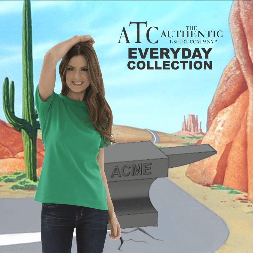 Smiling woman wearing a green short-sleeve t-shirt and dark jeans standing in front of a desert cartoon background with cactus and an anvil labeled ACME, promoting The Authentic T-Shirt Company's Everyday Collection