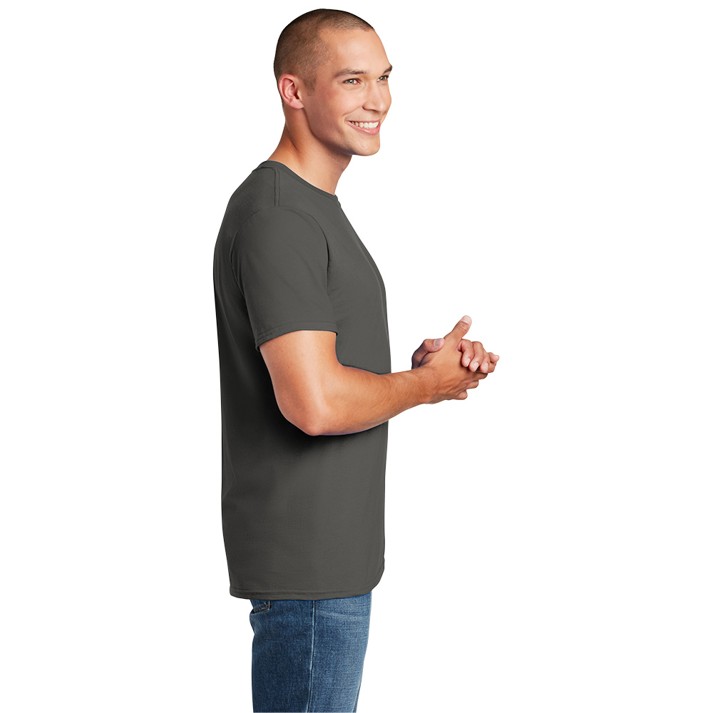 64000_charcoal_model_side Smiling young man with a shaved head wearing a dark gray short-sleeve t-shirt and blue jeans, standing in profile with hands clasped against a white background