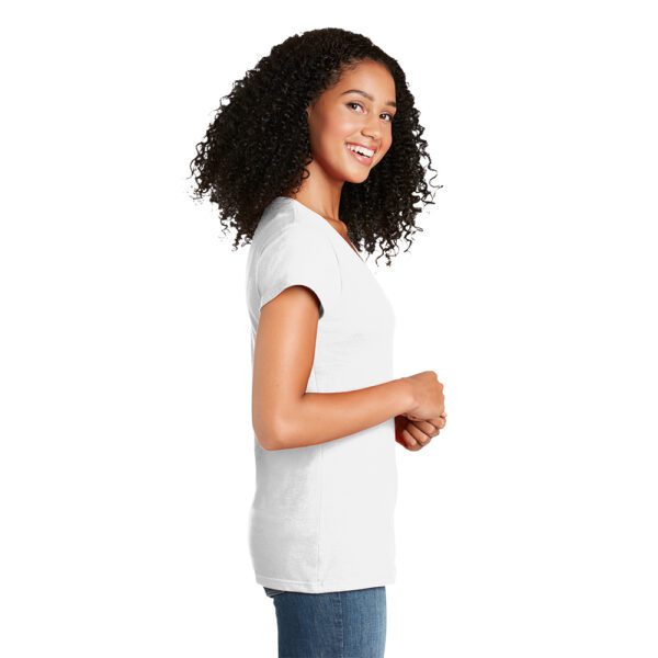 Smiling woman with curly hair wearing a plain white T-shirt and blue jeans, standing in profile with hands clasped.