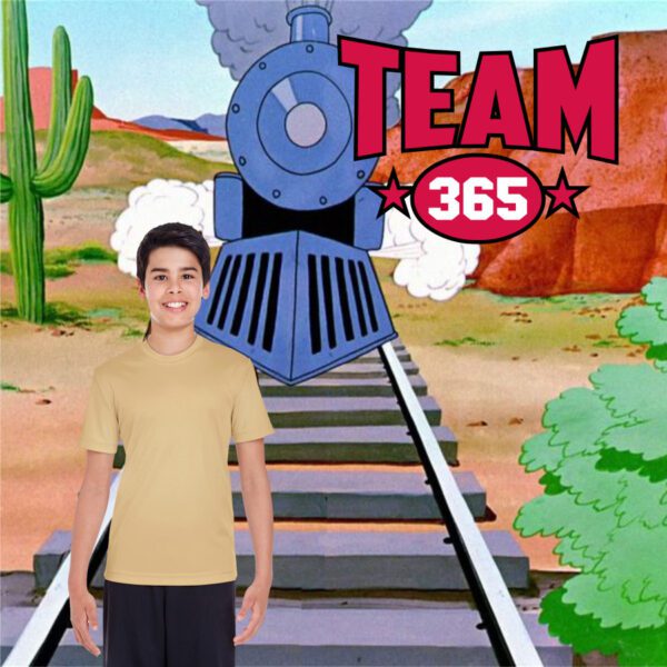 Young boy wearing a plain beige short-sleeve t-shirt and black shorts standing in front of a cartoon train on railway tracks with a desert background and 'TEAM 365' logo.