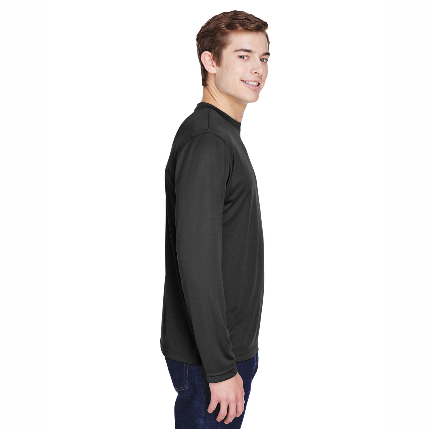 Side view of a young man with short brown hair wearing a long-sleeve black shirt and dark blue jeans, smiling against a white background.