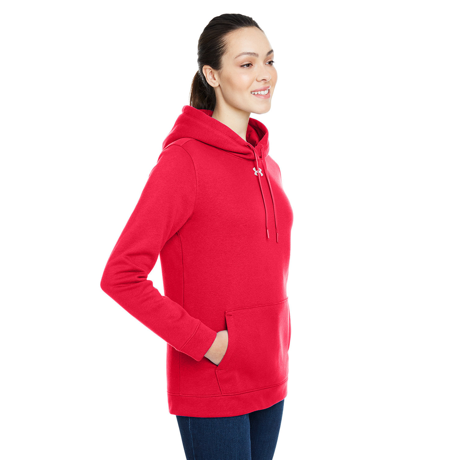 ua_ladies_cover_hustle_hoodie_front Smiling woman with dark hair tied back wearing a bright red Under Armour hoodie with a front pocket and dark blue jeans, standing against a white background.