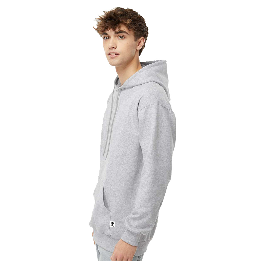 Young man wearing a light gray hoodie with a front pocket, standing in profile against a white background. The hoodie features a drawstring and a small logo tag at the bottom.