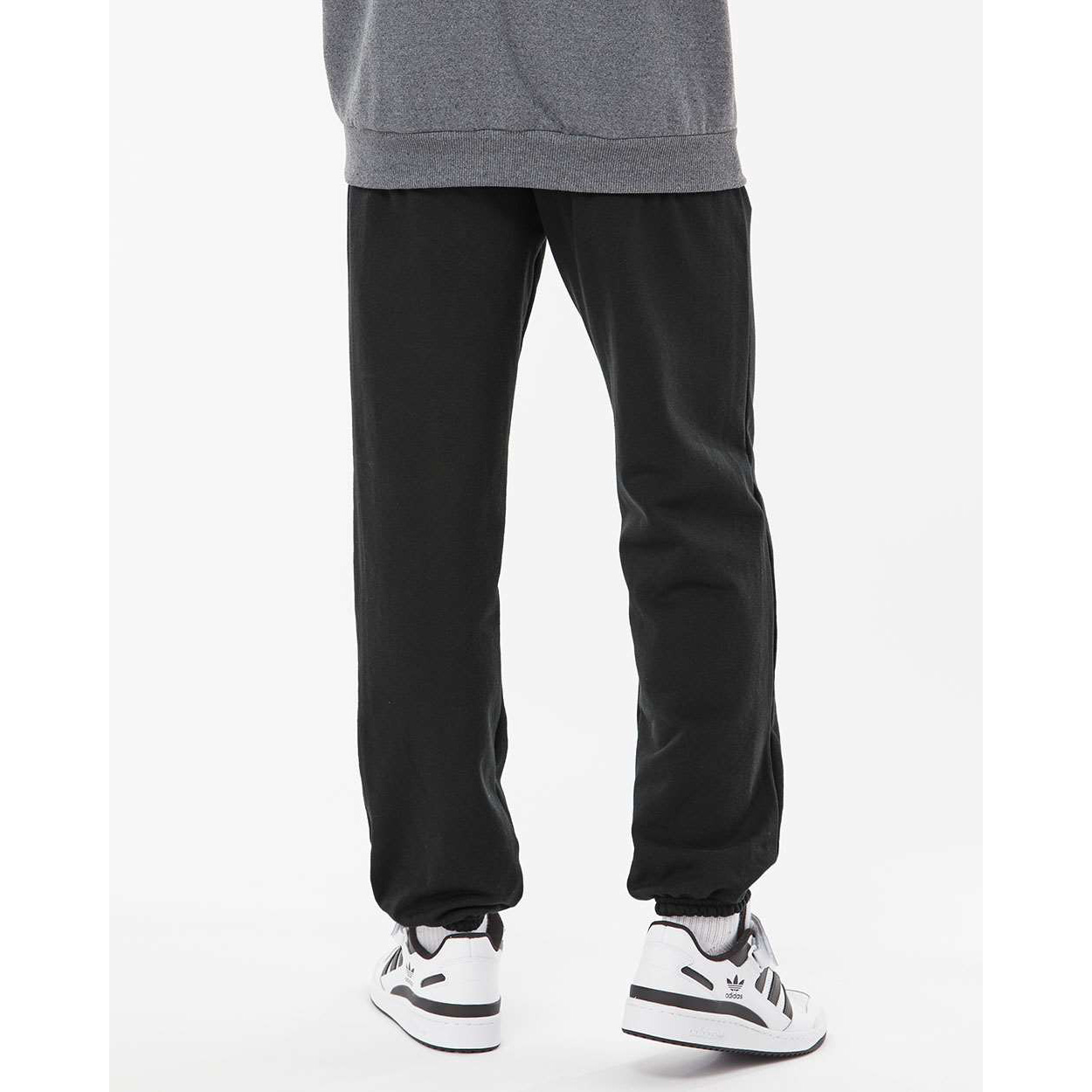 Lower half of a person wearing black jogger pants with elastic cuffs and white Adidas sneakers, standing against a plain white background.