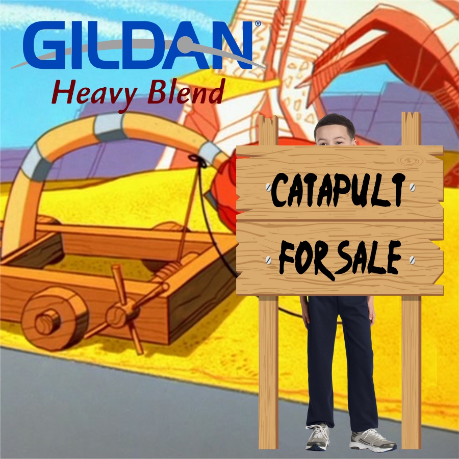 Animated scene with a wooden catapult on a yellow surface, a boy stands behind a wooden sign that reads 'CATAPULT FOR SALE', the boy's face partially visible above the sign and legs visible below, GILDAN Heavy Blend logo in the upper left corner