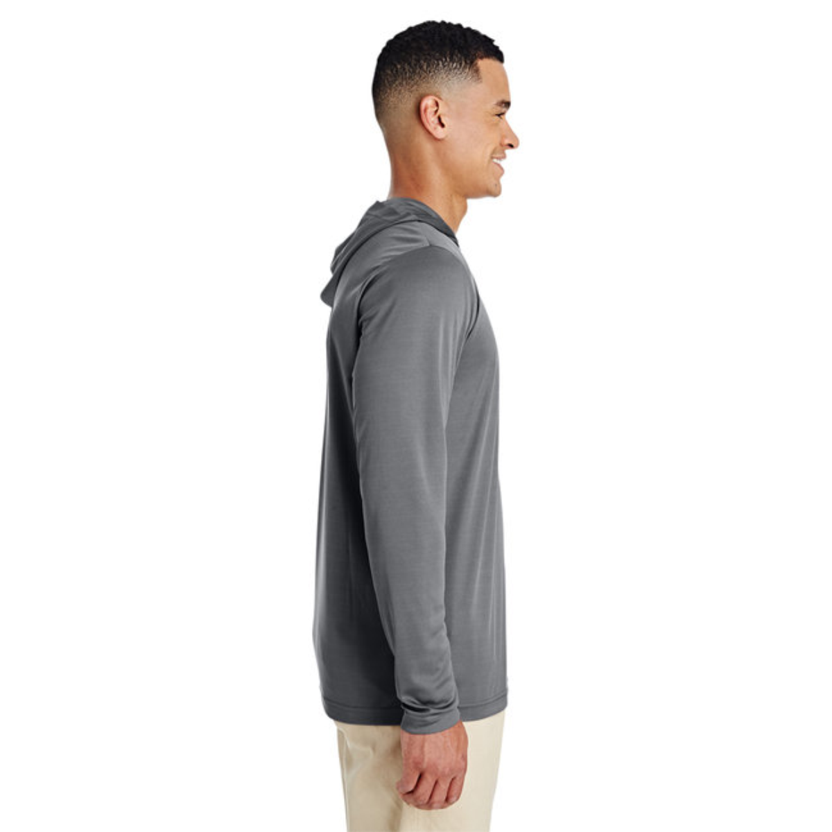 Side view of a man smiling, wearing a gray long-sleeve hooded shirt and light-colored pants against a white background.