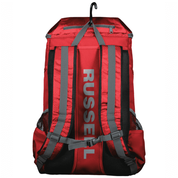Red backpack with grey straps, black mesh padding, a zipper pocket on top, and the word RUSSELL printed vertically in grey on the back panel, hanging on a black hook.