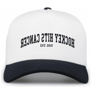 White and navy baseball cap featuring the phrase "Hockey HITS Cancer" and the establishment year "EST. 2015," promoting cancer awareness through hockey-themed merchandise.
